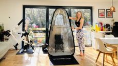 a woman stands next to a pop-up sauna pod in her home