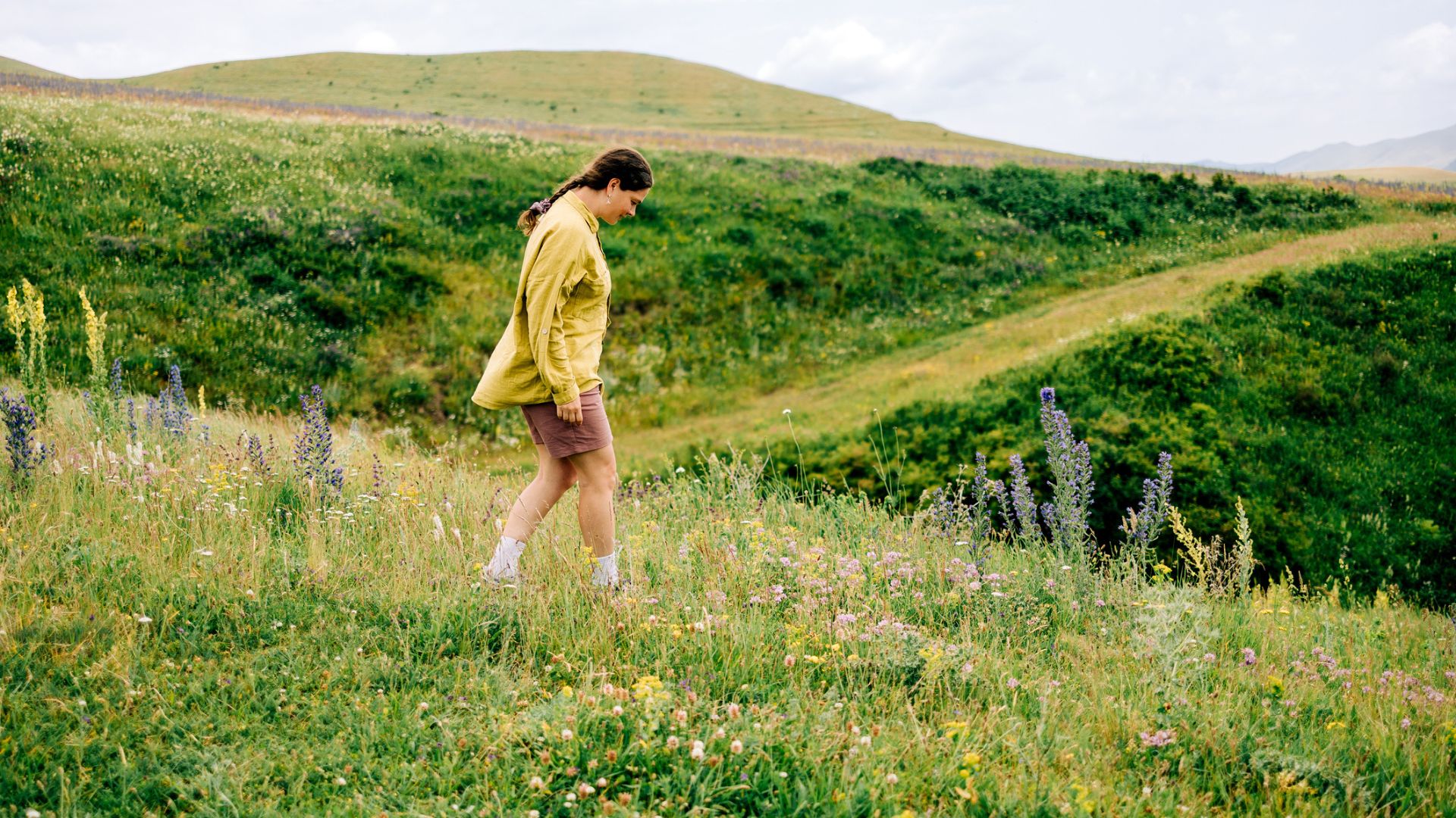 woman in shorts and shirt walks down a hill in the countryside