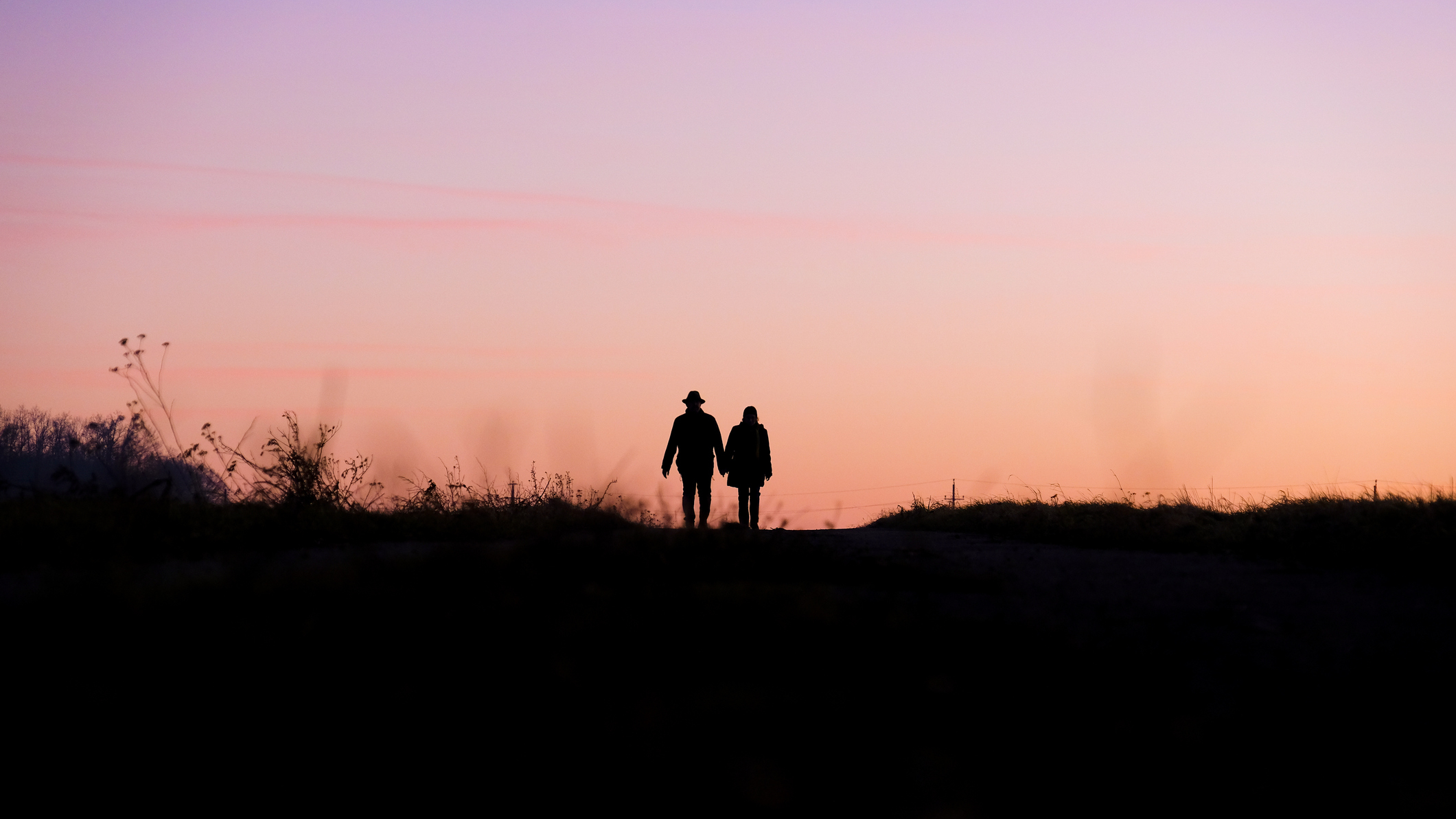 Silhouette of two people walking together against a pink sky