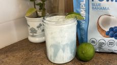 Mason jar of white liquid garnished with lime wedge. It is on a countertop next to a plant pot, whole lime, and packet of unidentified food