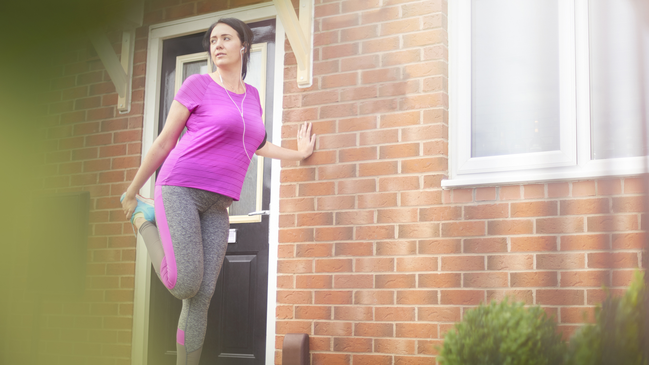 Woman in running clothes stretches outside a front door
