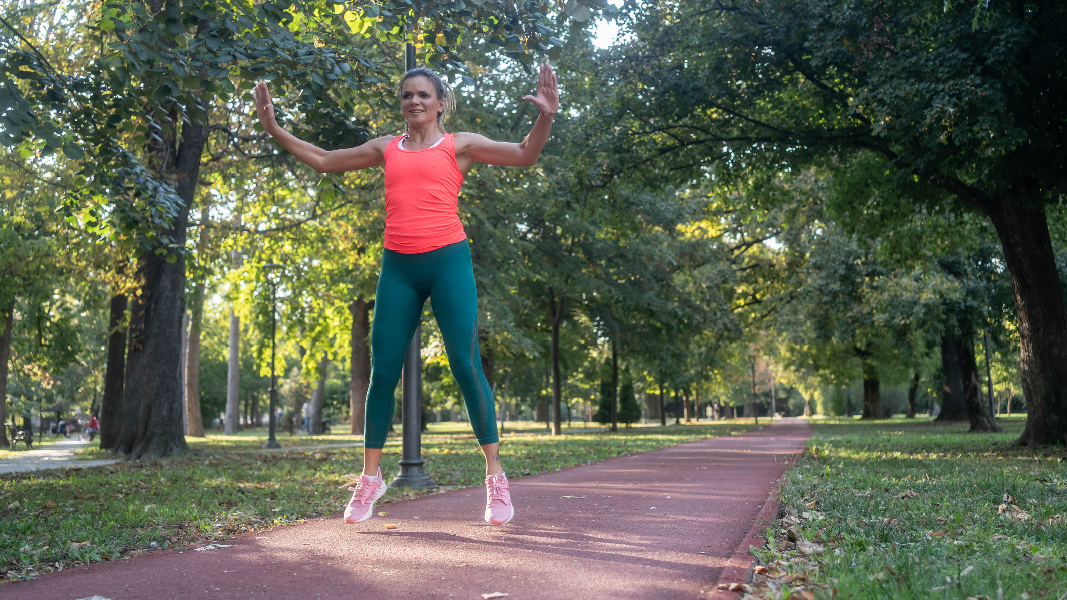 Woman in sportswear jumping in midair on park path