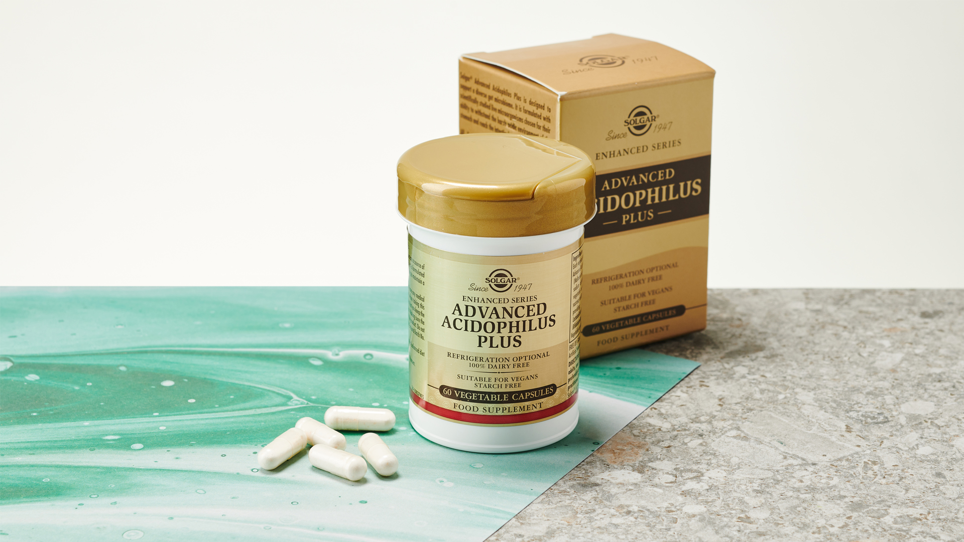 A Solgar Advanced Acidophilus+ probiotic box and plastic tub with capsules next to them on a marble surface
