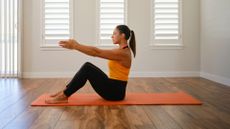 woman sits on yoga mat with arms extended in front while engaging her core