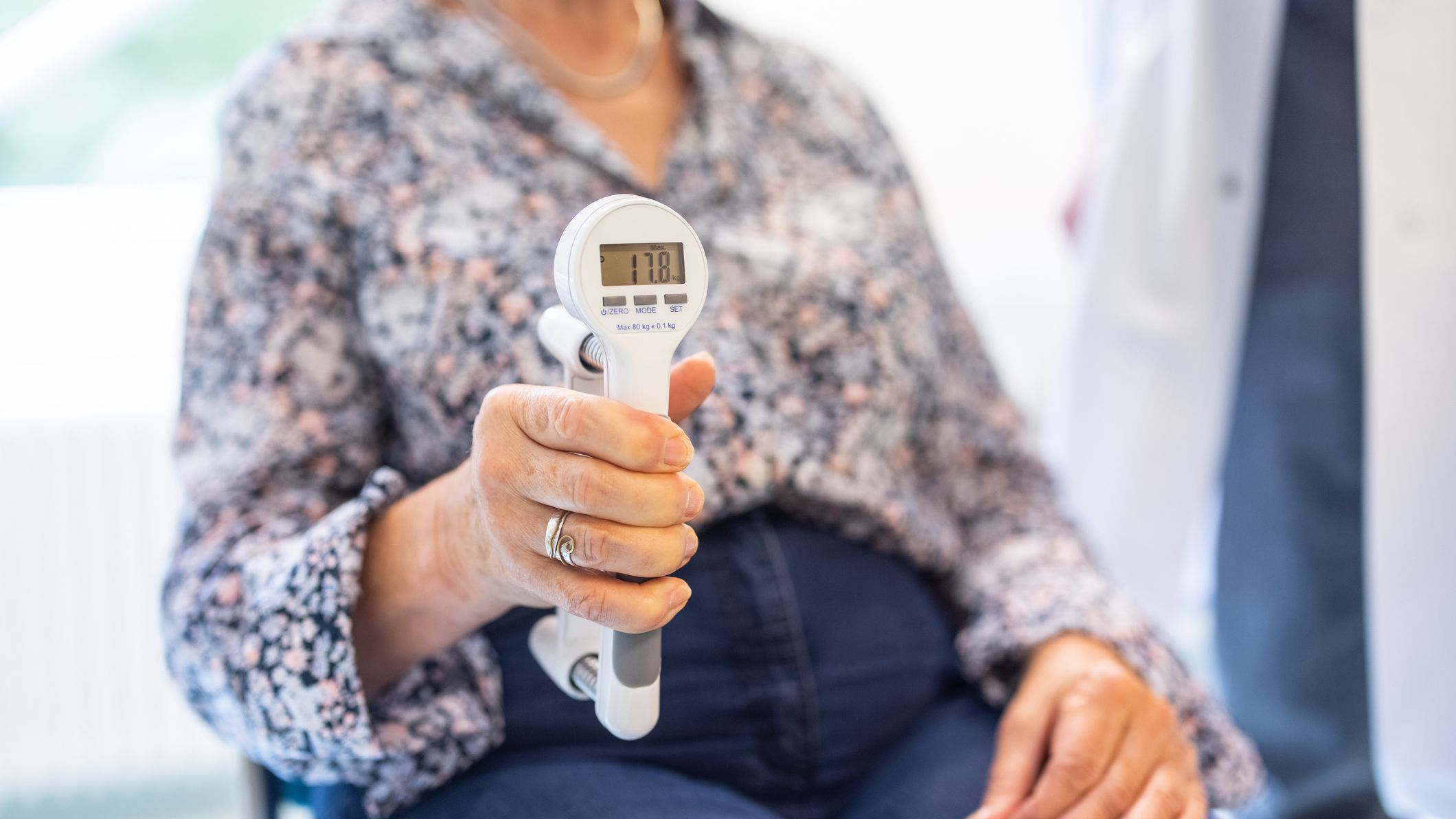 Close-up of a senior woman using hand dynamometer for grip strength test in clinic.
