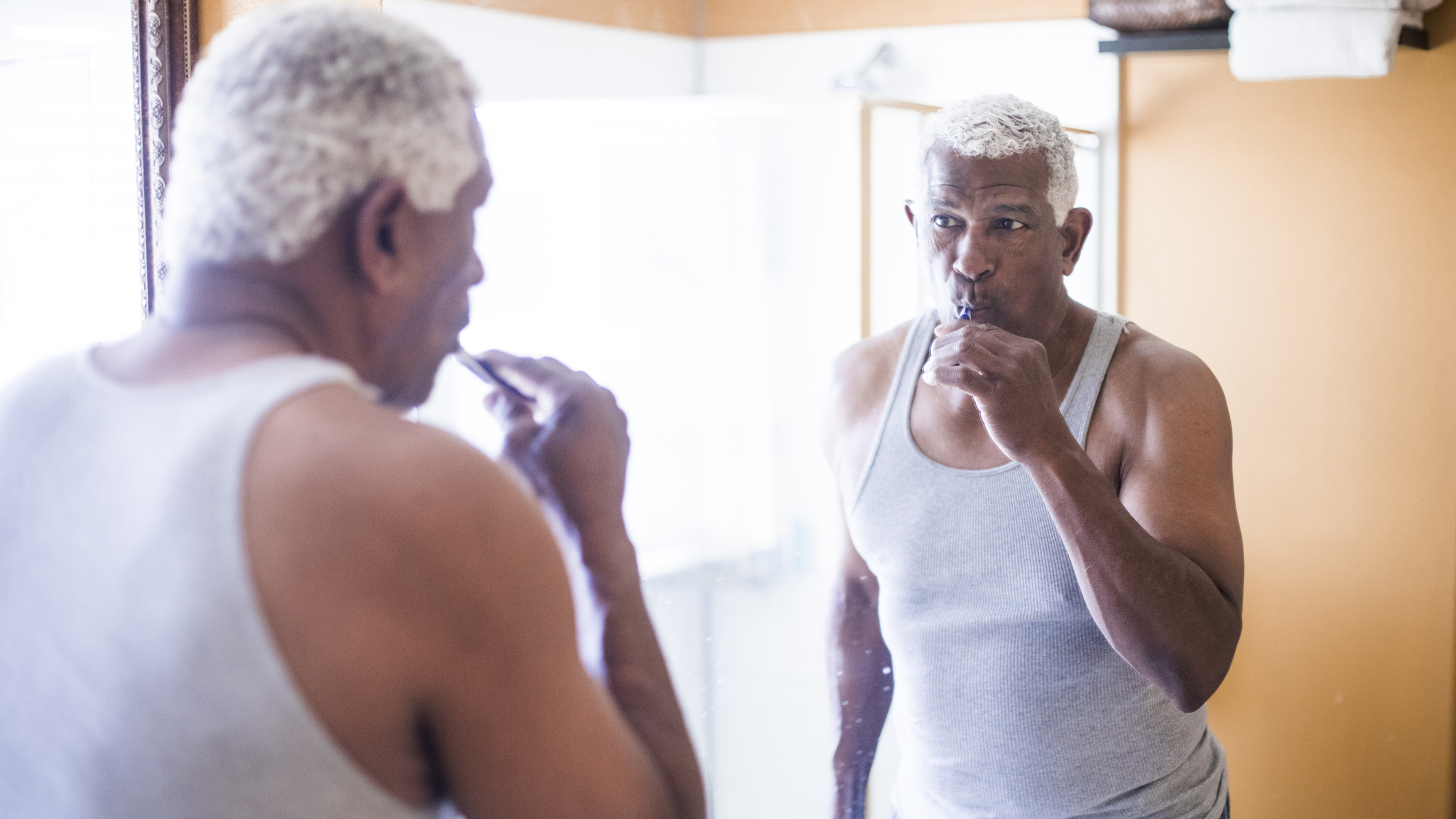 Man brushing his teeth and looking at his reflection in a bathroom mirror