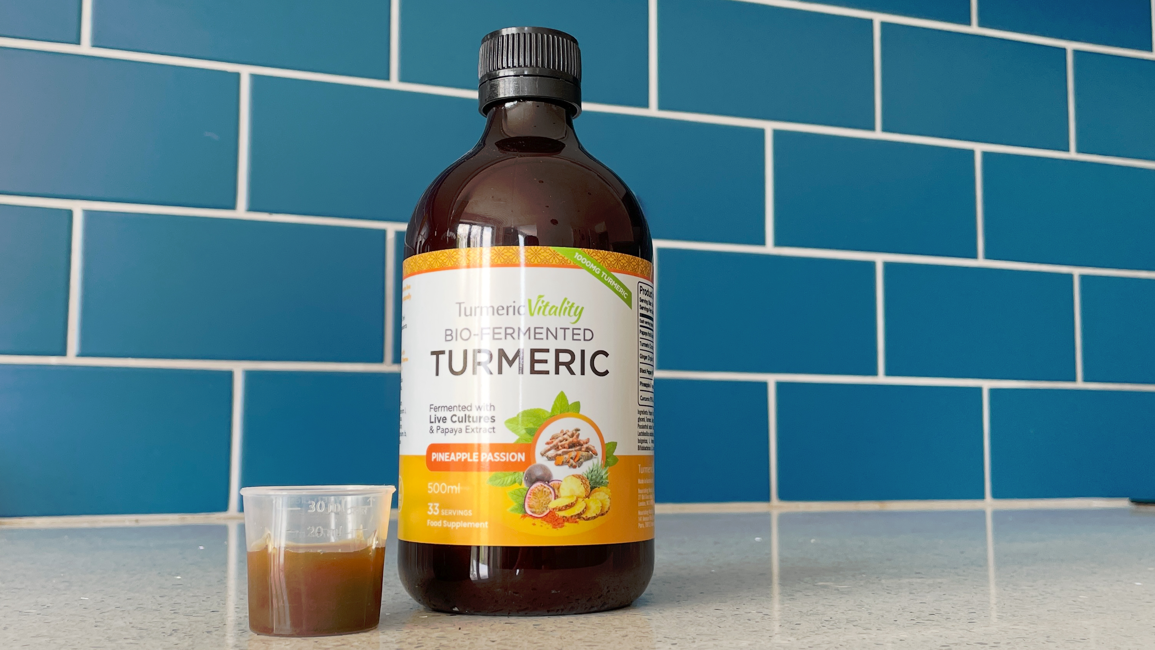 A bottle of Turmeric Vitality Bio-Fermented Turmeric with a shot of it in a plastic cup on a kitchen top