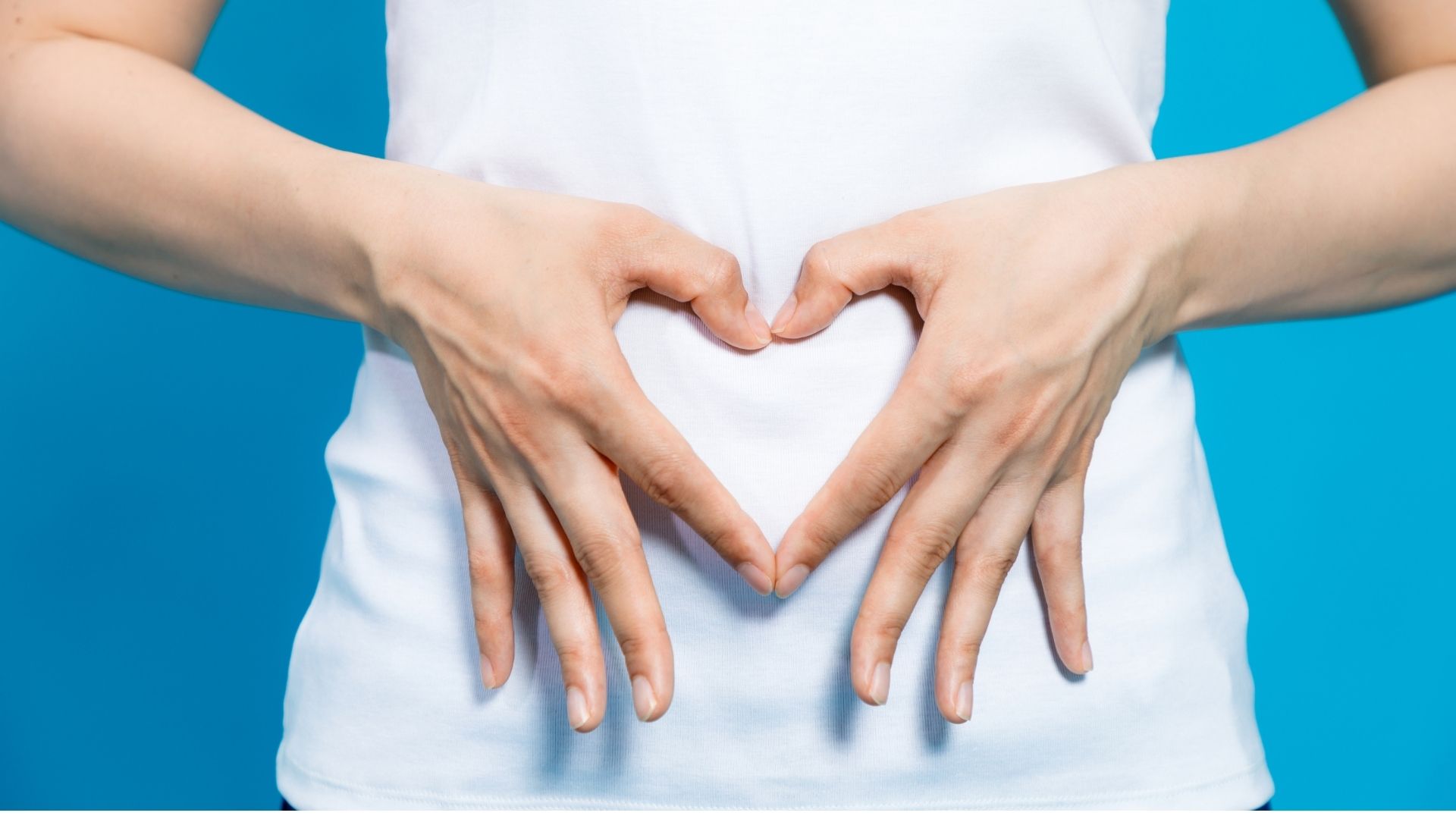 Close up of a woman in white t-short with her fingers creating a heart symbol over her stomach area