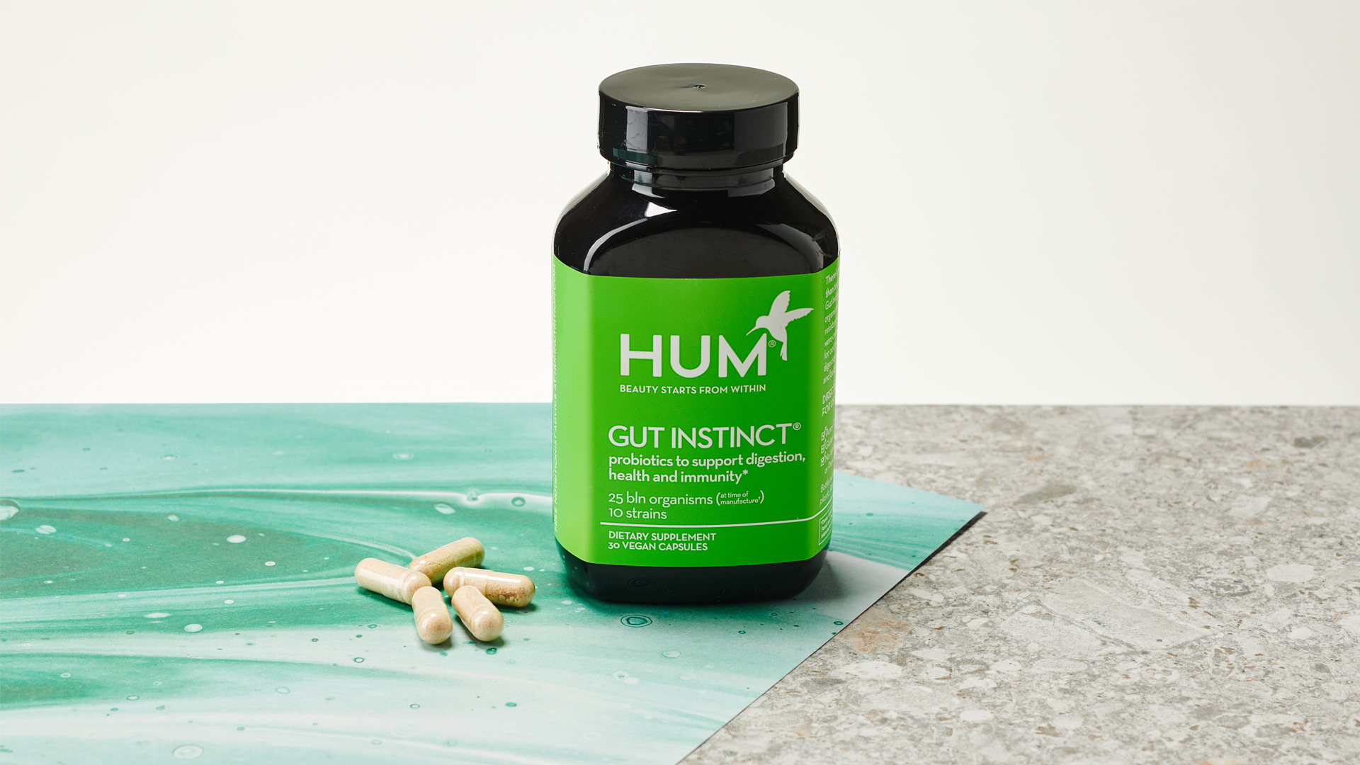 A bottle of Hum Nutrition Gut Instinct on a marble surface with some capsules next to it