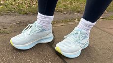 A pair of Saucony Ride 18s in eggshell blue being worn outside on a concrete path by fitness writer Alice Porter.